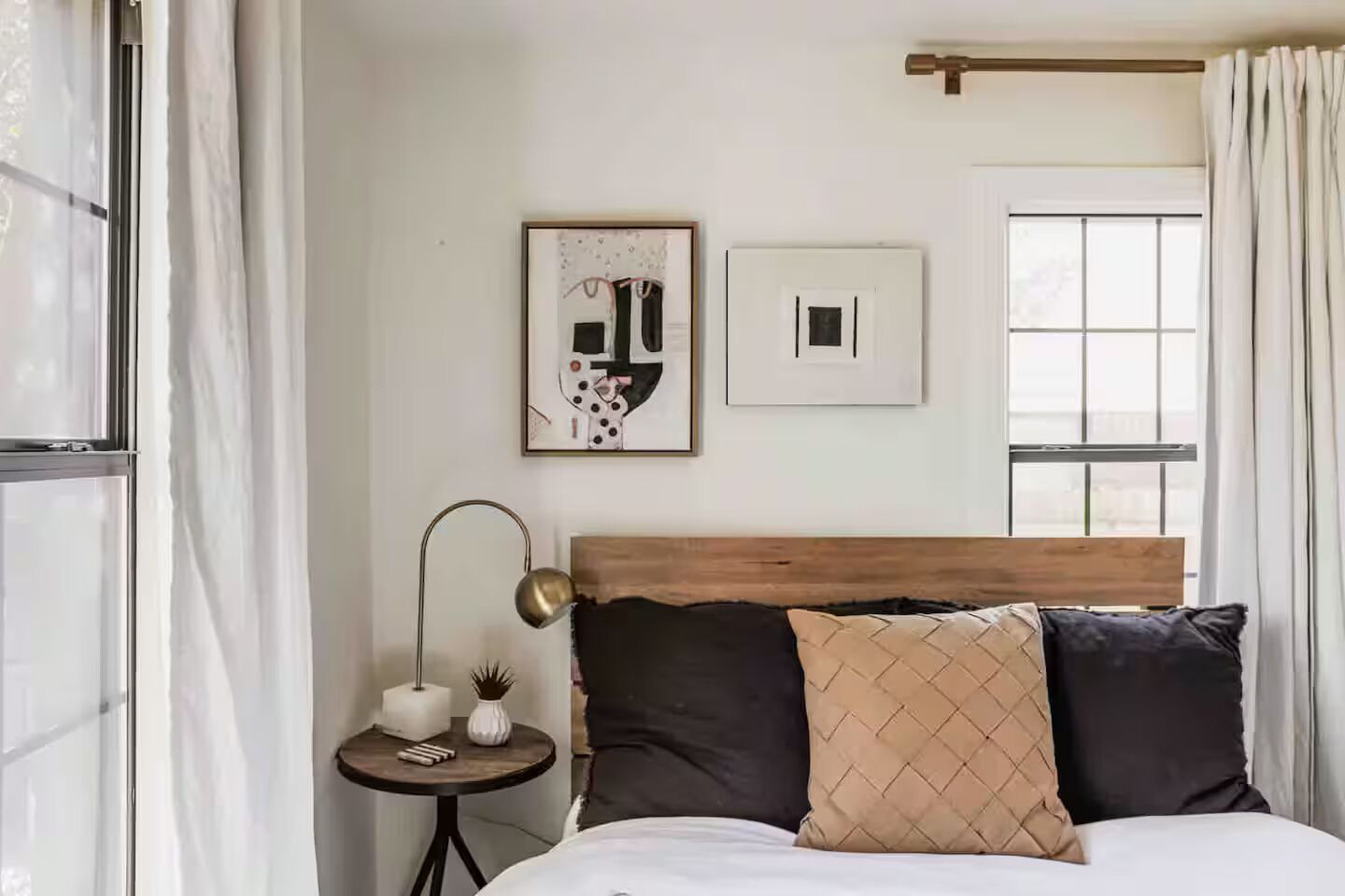 Un dormitorio con cabecera de madera, una mesita de noche con lámpara y dos obras de arte enmarcadas en la pared.