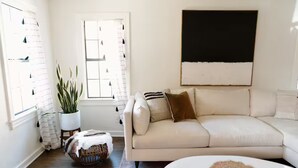 A living room with a beige sofa, a white coffee table, and a large window with curtains. - Cozy Historical Home, Walk to Downtown Edmond (Edmond)