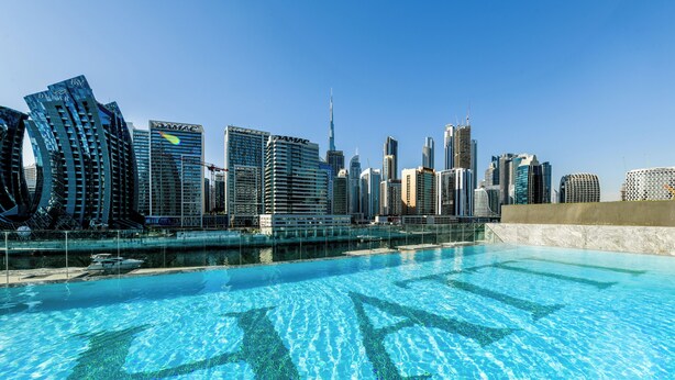 A swimming pool with cityscape views, including modern skyscrapers and a distinctive curved building. - Chic 1BR with Private Terrace & Burj Khalifa Skyline View | 4 Guests (Dubai)