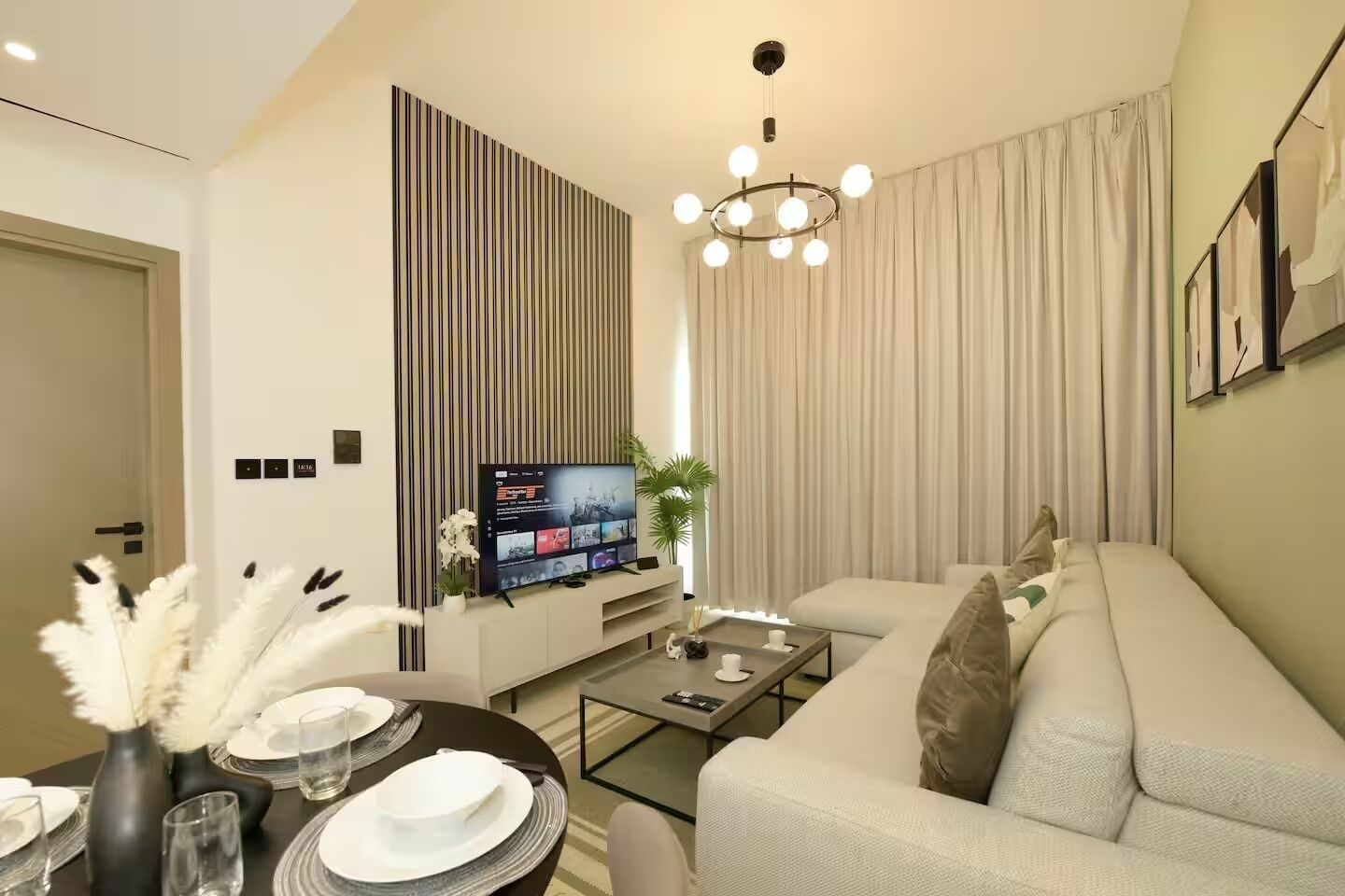 A modern living room with a flat-screen TV, a sofa, a coffee table, and a dining area with a table set for two.
