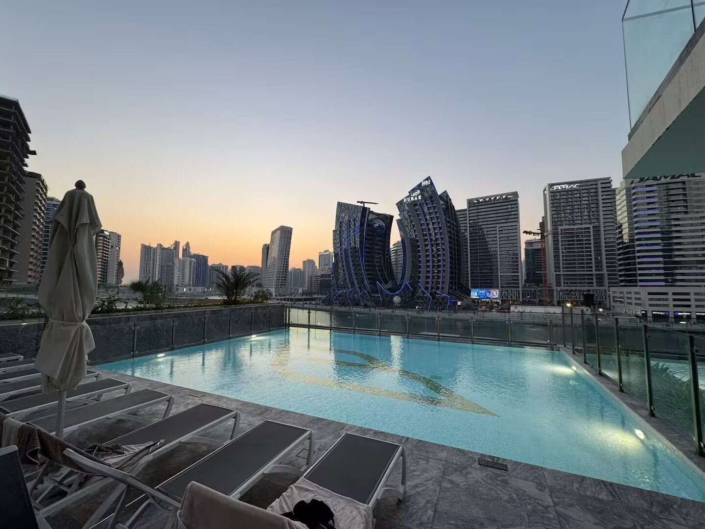A rooftop pool with lounge chairs and a city skyline in the background.