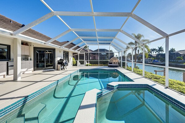 A swimming pool with a covered patio area, a view of the water, and a building with a tiled roof. - Marco Island Waterfront Home w/ Pool & Boat Dock (Marco Island)