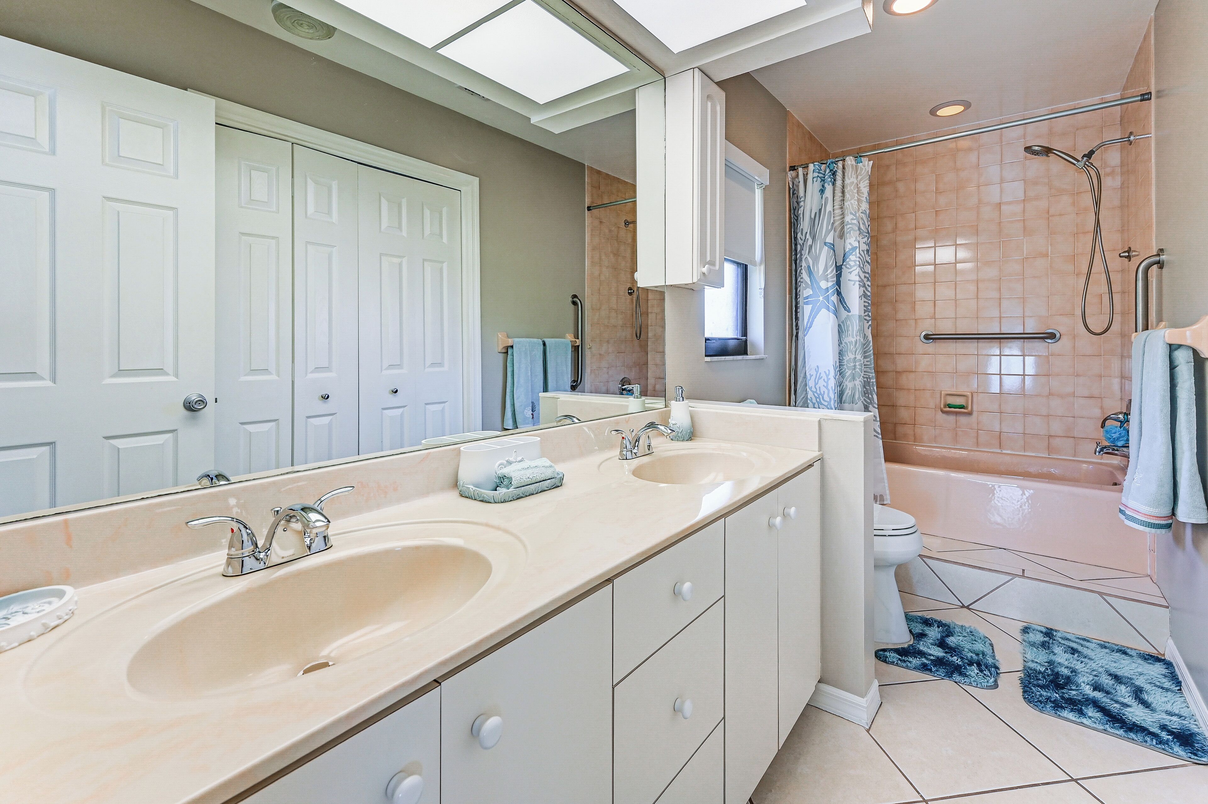 A bathroom with a large mirror, two sinks, a shower, and a toilet.