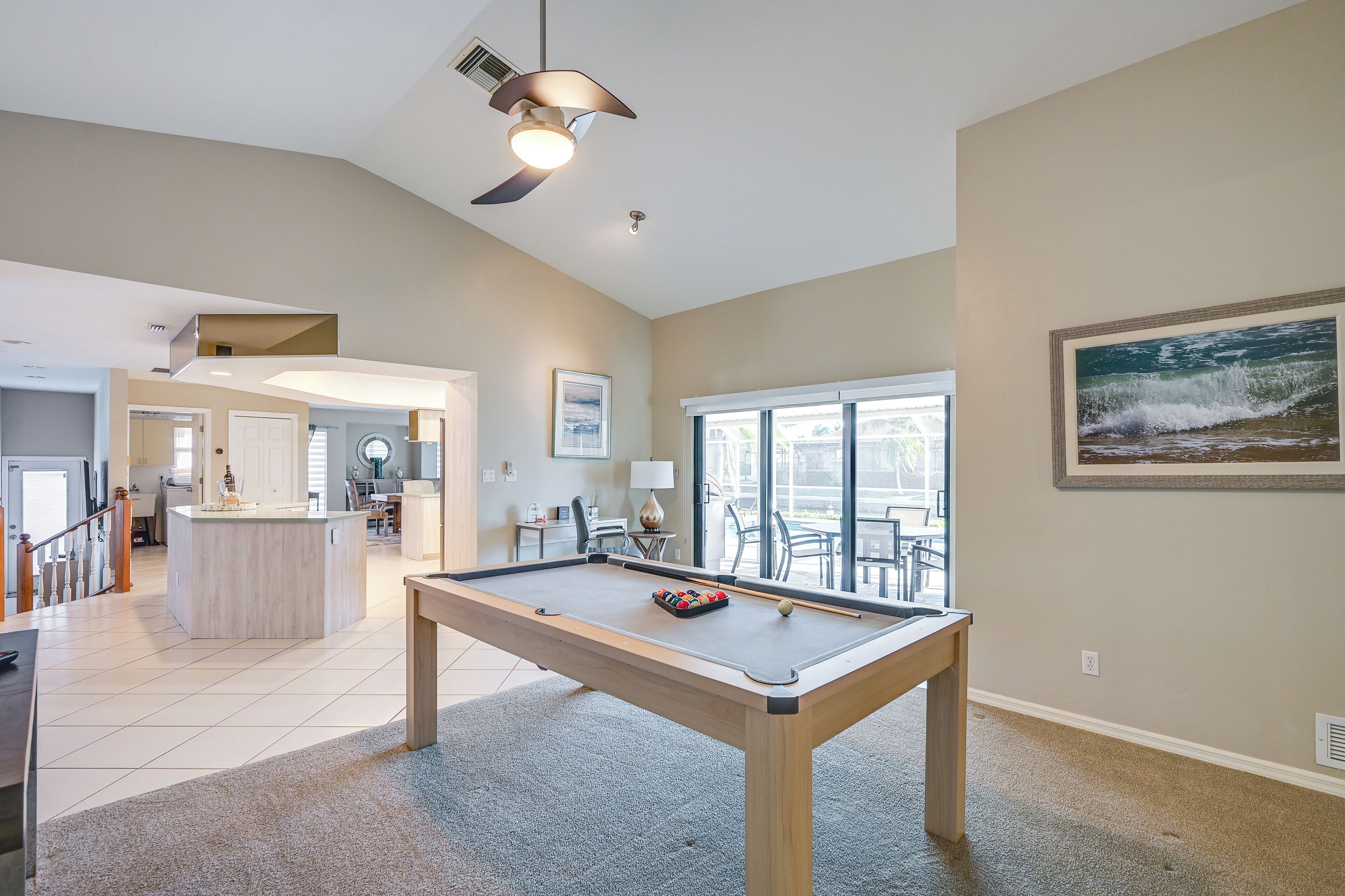 A spacious room with a pool table, a ceiling fan, and a large window providing a view of the outdoors.