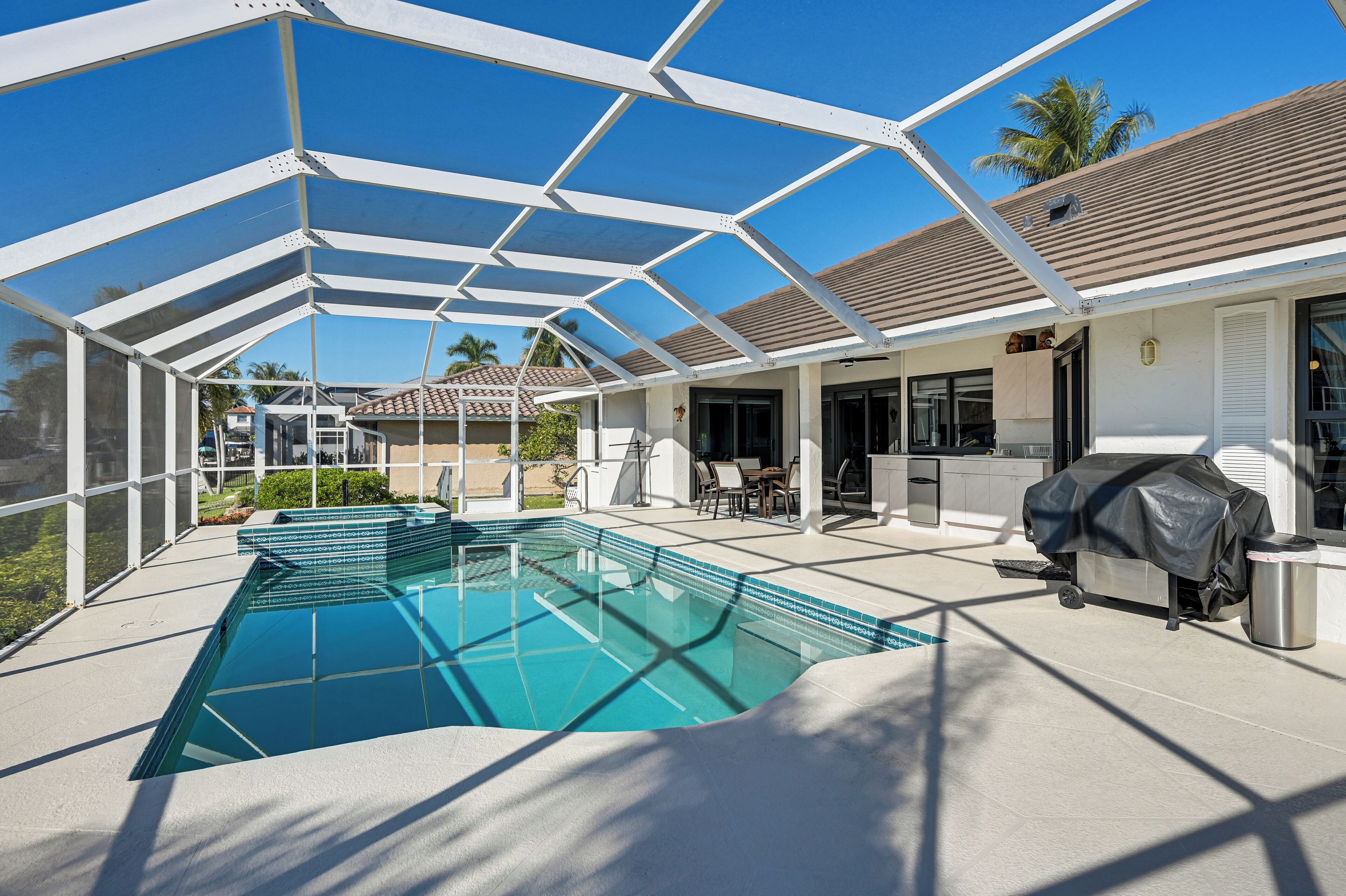 Une piscine extérieure couverte, dotée d’un espace patio, d’un barbecue et offrant une vue sur les maisons voisines.