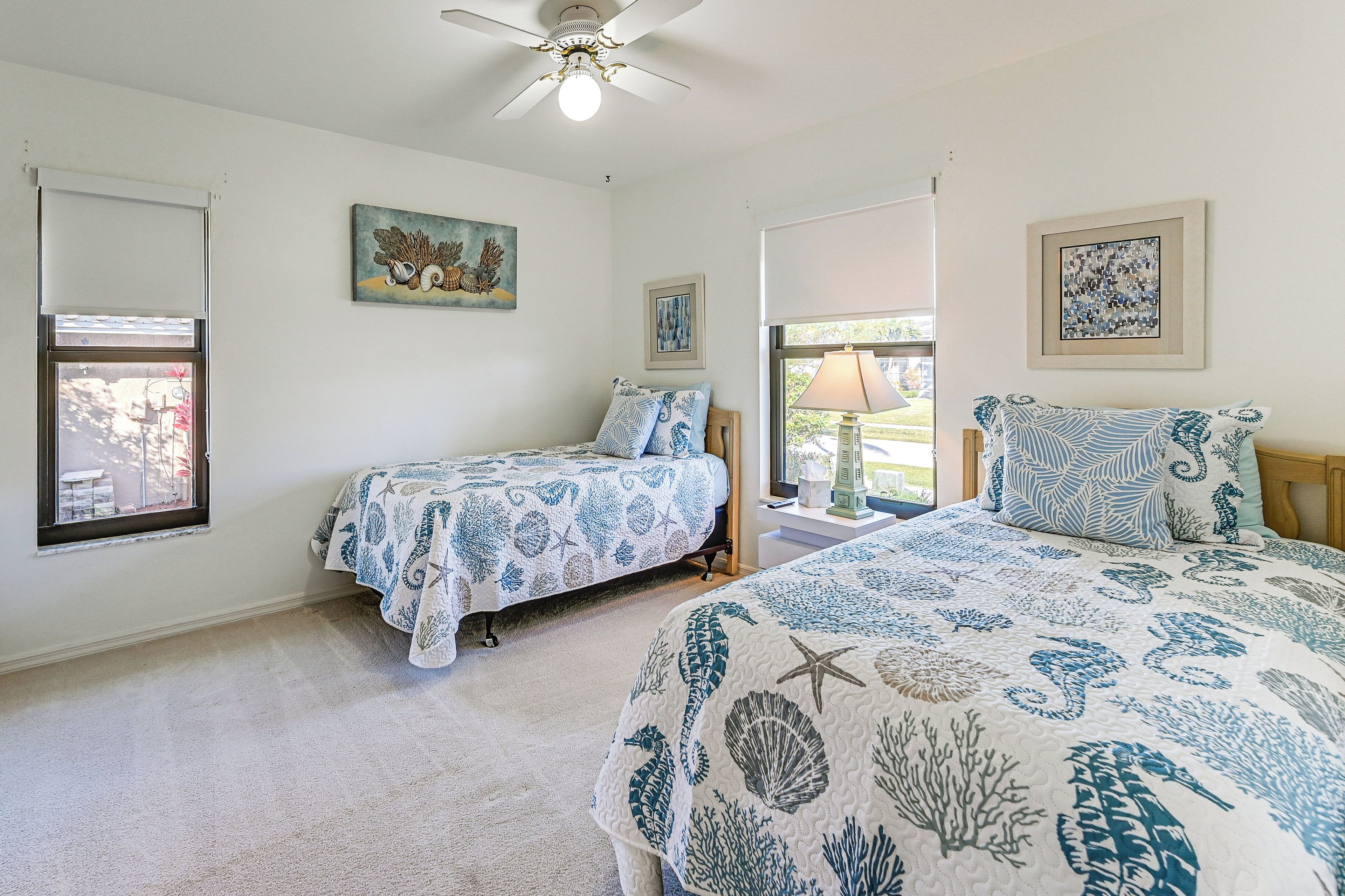 A bedroom with two beds, a ceiling fan, and artwork on the walls.