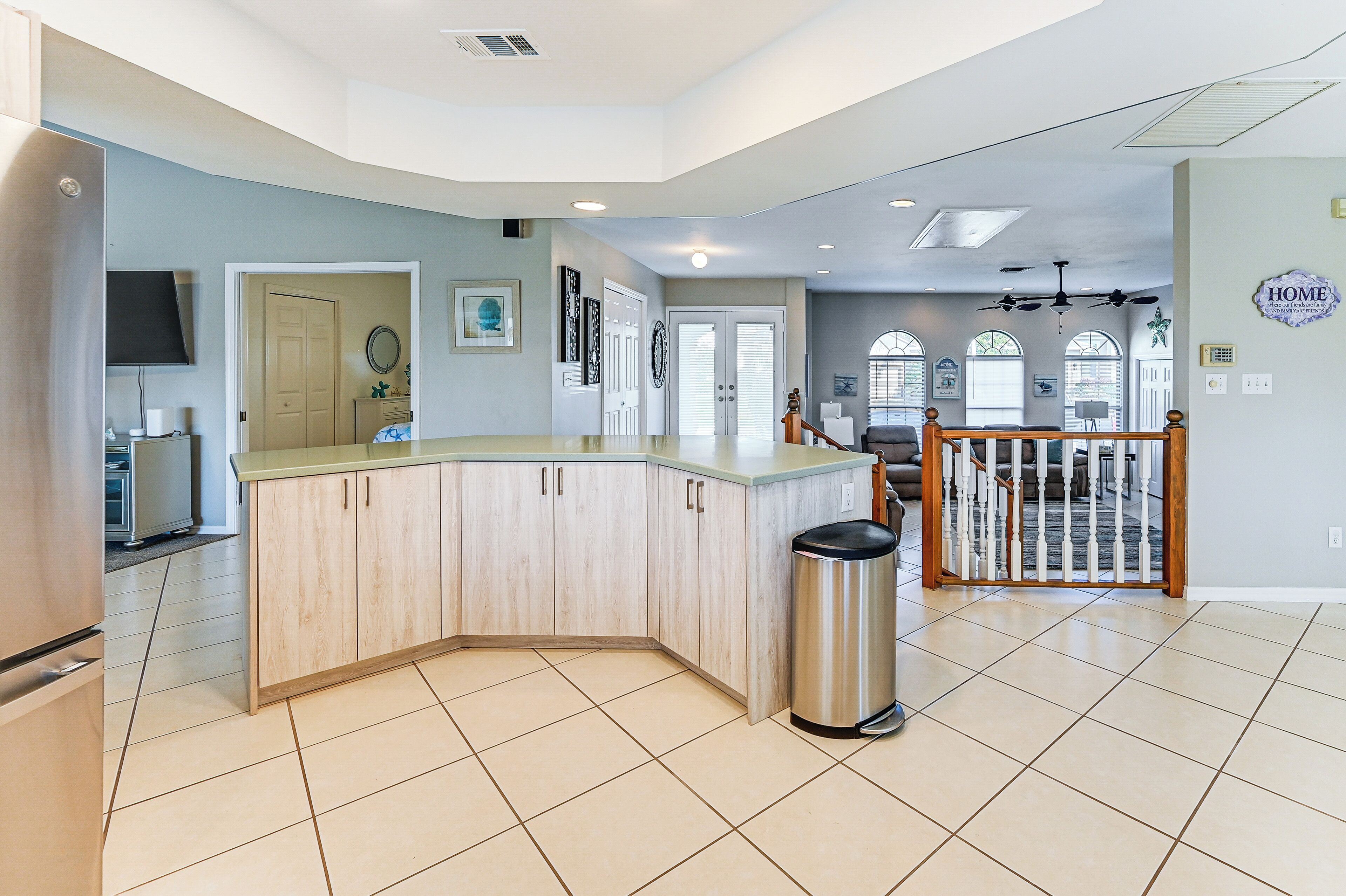 A spacious kitchen with a central island, a dining area with a wooden railing, and a view of the living room through a glass door.
