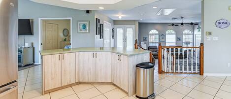 A spacious kitchen with a central island, a dining area with a wooden railing, and a view of the living room through a glass door.
