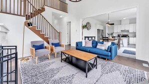 A spacious living area with a staircase, a blue sofa set, a wooden coffee table, and a chandelier. - Spacious & New Prince Edward County Family Home (Quinte West)