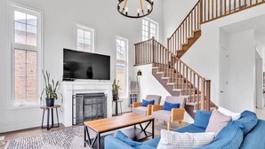 A living room with a fireplace, a TV, a staircase, and a blue sofa. - Spacious & New Prince Edward County Family Home (Quinte West)