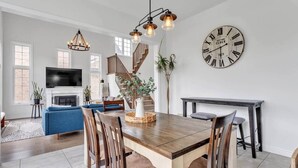 A spacious living room with a wooden dining table, blue sofa, and a staircase leading to another level. - Spacious & New Prince Edward County Family Home (Quinte West)