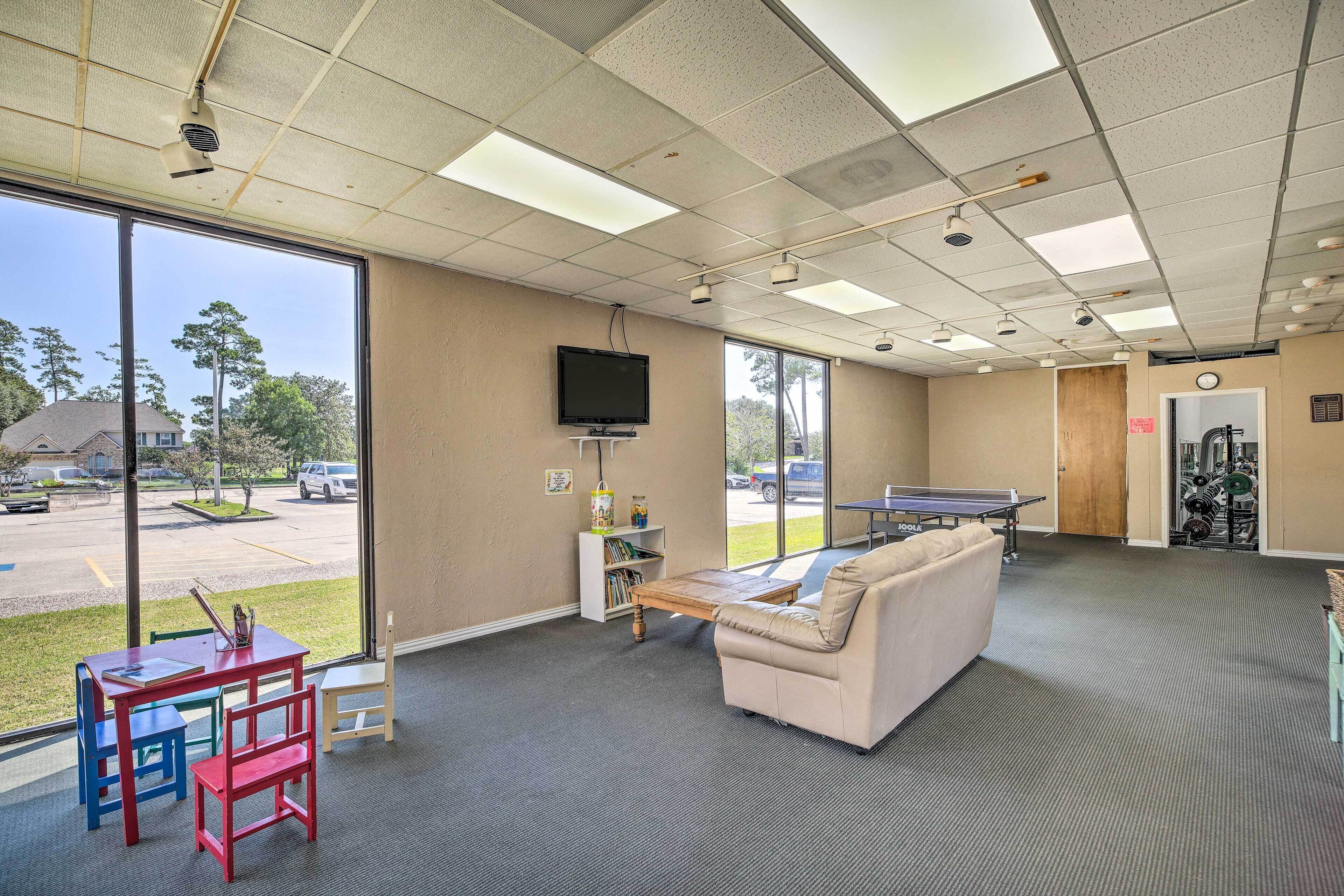 A spacious room with a large window, a flat-screen TV, a ping pong table, and a sofa.