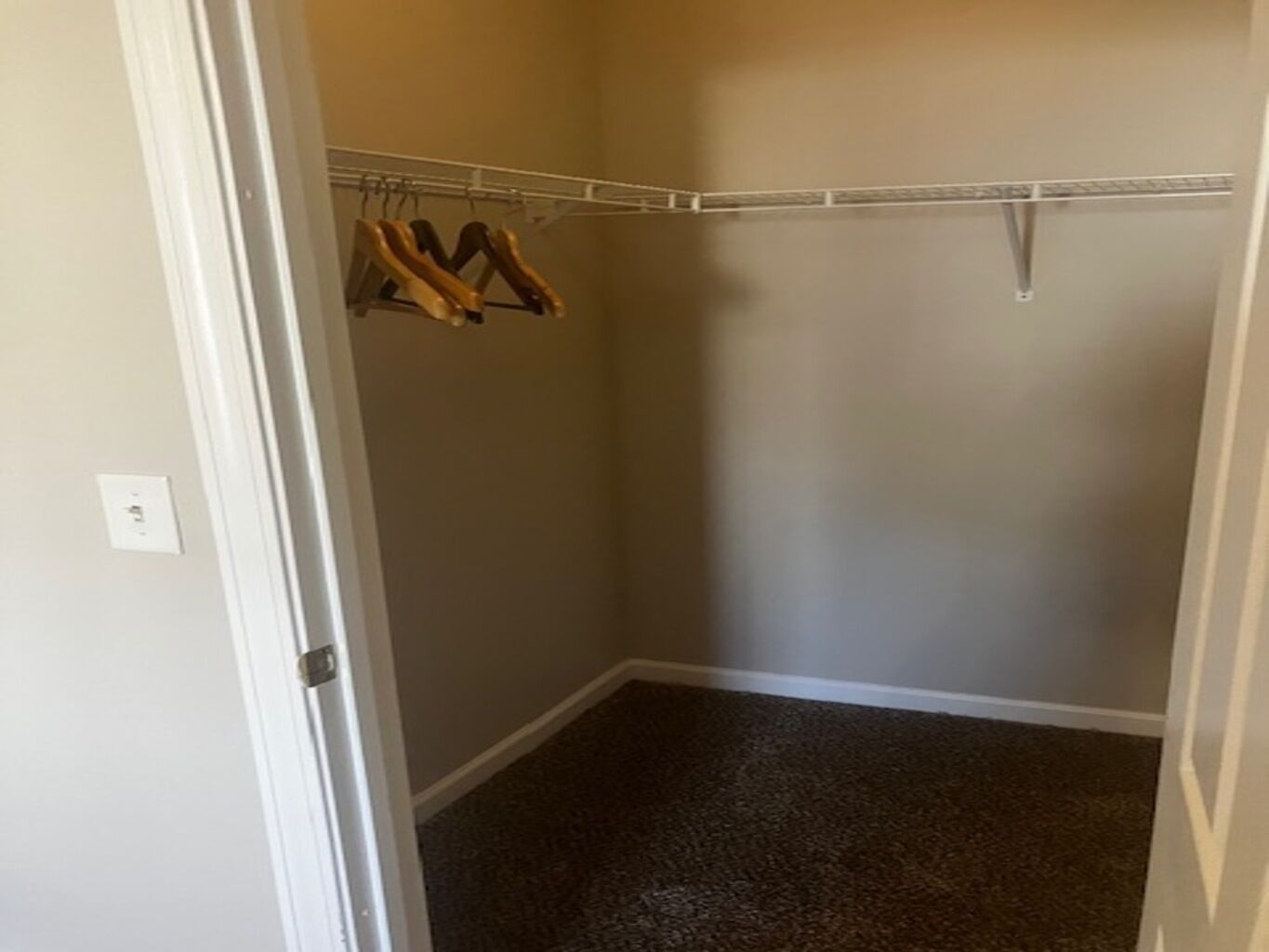 A walk-in closet with a metal rod rack holding several wooden hangers.
