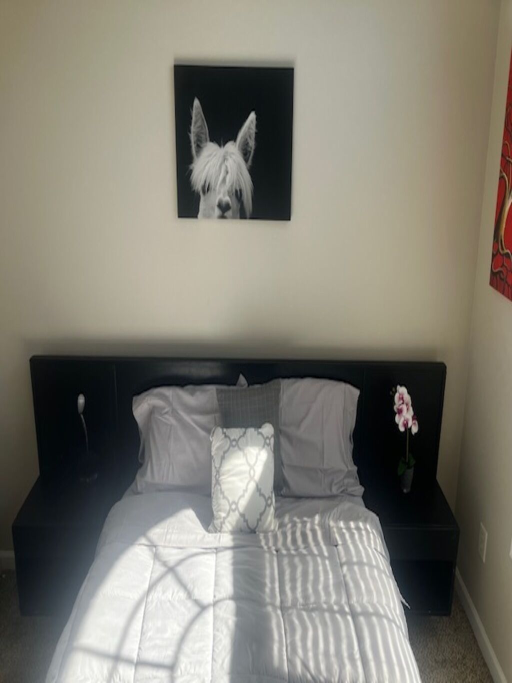 A bedroom with a bed, pillows, a bedside table, and a framed picture on the wall.