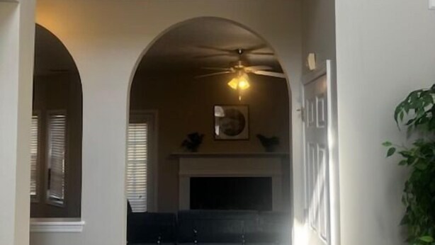 A hallway with a ceiling fan, a fireplace, and a view into a kitchen area. - Sleek Chateau Residence: 4BR Modern Hideaway in Jonesboro (Jonesboro)