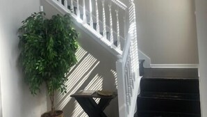 A staircase with white balusters, a potted plant, and a small table with a book. - Sleek Chateau Residence: 4BR Modern Hideaway in Jonesboro (Jonesboro)