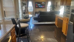 A modern kitchen with a dining area, a living room with a sofa, and a TV. - Sleek Chateau Residence: 4BR Modern Hideaway in Jonesboro (Jonesboro)
