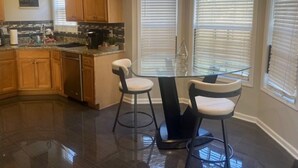 A kitchen with wooden cabinets, a granite countertop, a glass dining table with two bar stools, and a chandelier. - Sleek Chateau Residence: 4BR Modern Hideaway in Jonesboro (Jonesboro)