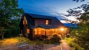 A rustic log cabin with a porch, a fire pit, and a bench.
