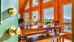 A wooden cabin interior with large windows, a dining table, and a view of the outdoors.