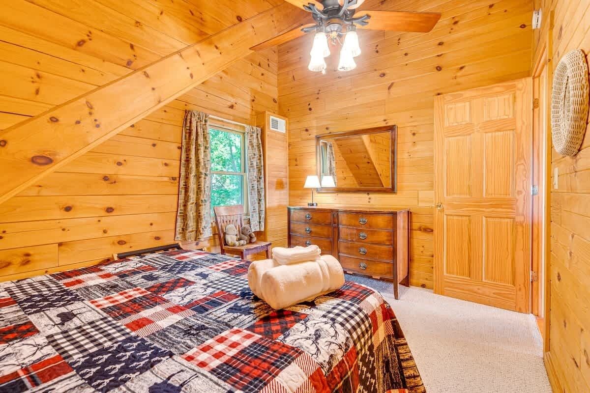 A wooden cabin bedroom with a bed, a dresser, a mirror, and a ceiling fan.
