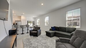 Una sala moderna con un sofá modular, una mesa de centro y un televisor sobre un mueble bajo. Hay cuatro sillas y una alfombra en el suelo.