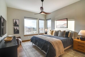 Ein Schlafzimmer mit Bett, Schreibtisch, Stuhl, Deckenventilator und großen Fenstern mit Blick auf die Stadt.
