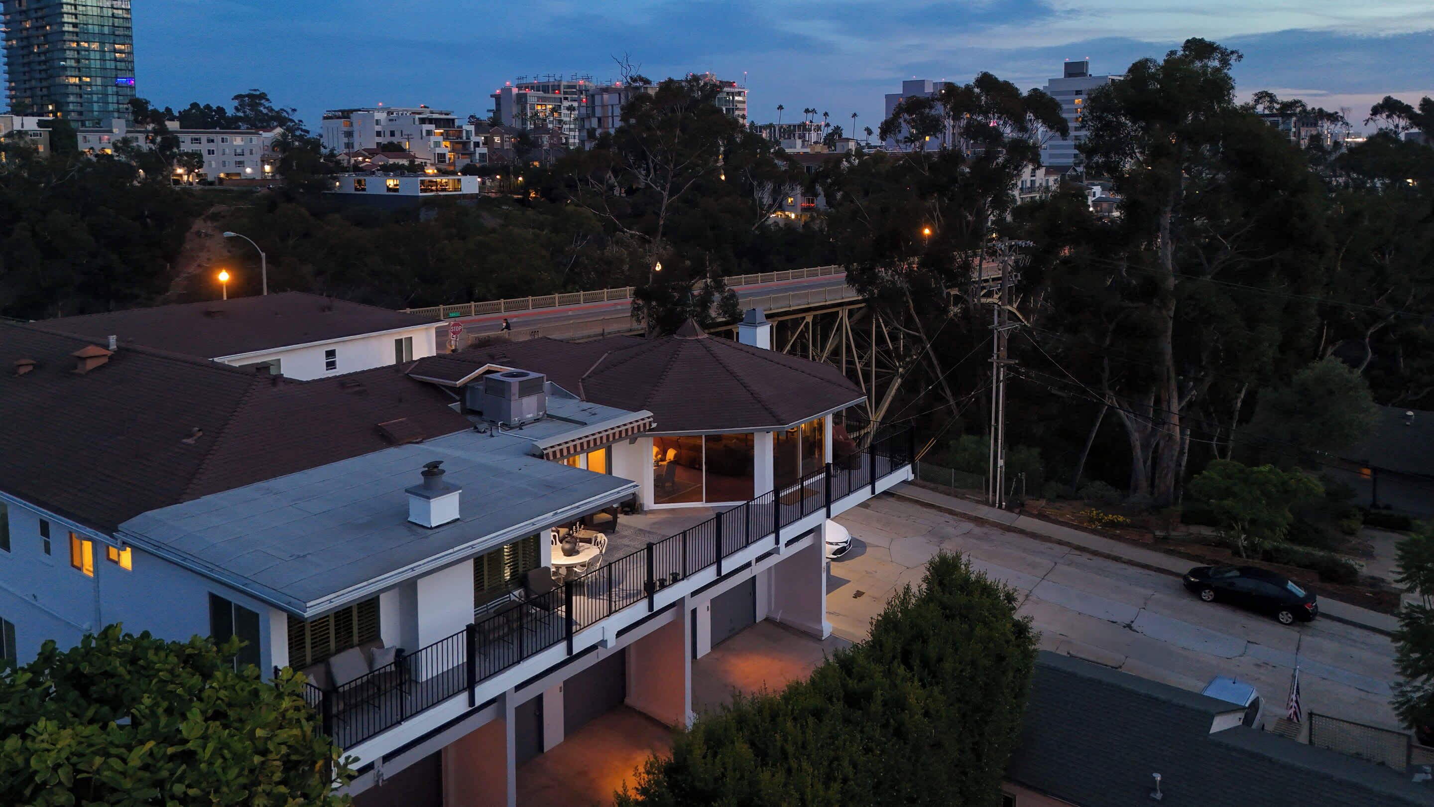 A residential building with a flat roof, a covered patio, and a view of a street and other buildings.