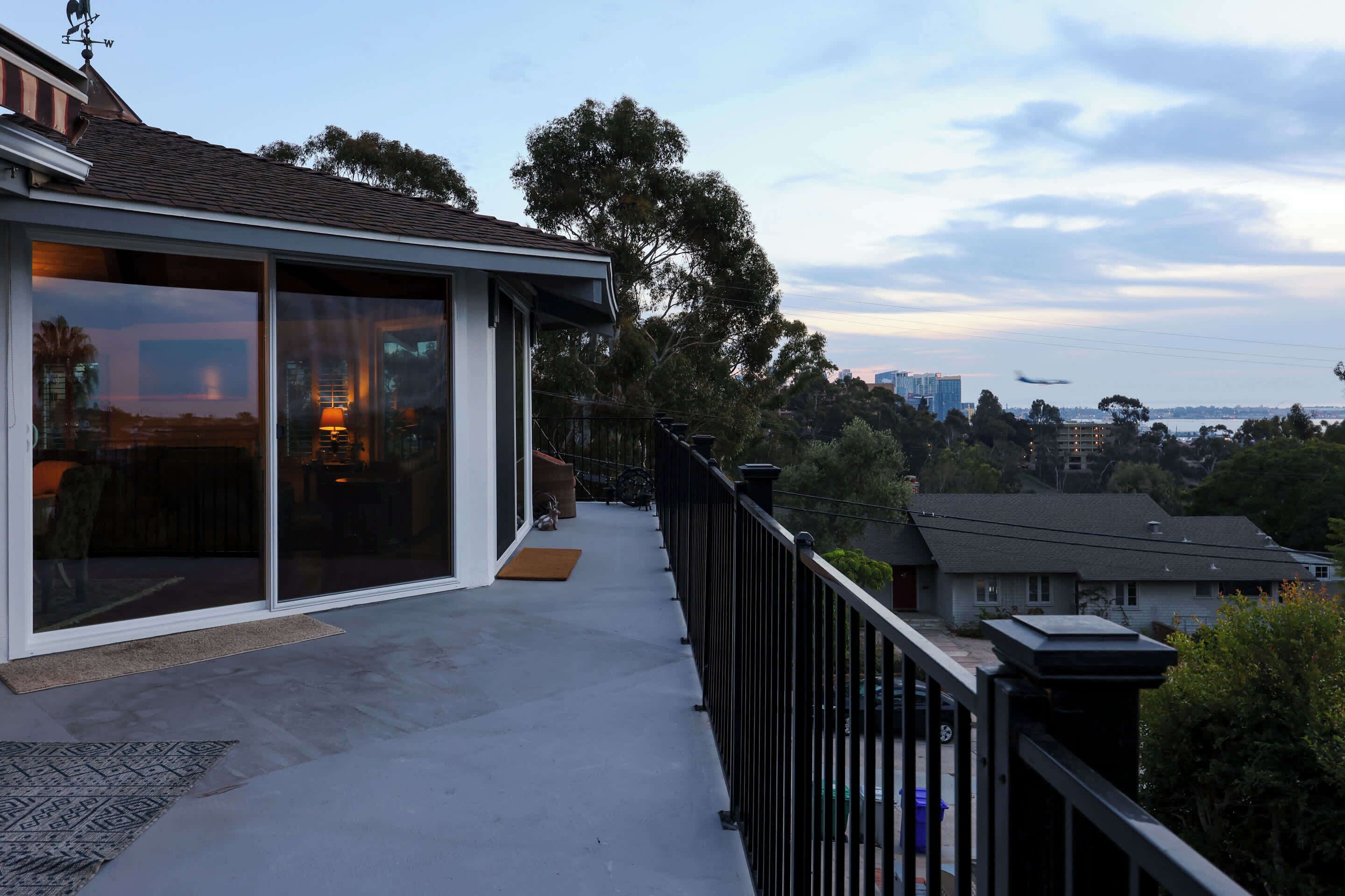 Uma casa moderna com varanda, grandes portas de correr de vidro e vista para a paisagem urbana e um avião ao longe.