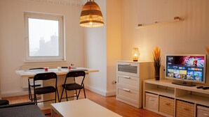 Ein modernes Wohnzimmer mit Essbereich, einem Fernseher und einem Fenster mit Blick auf Gebäude.