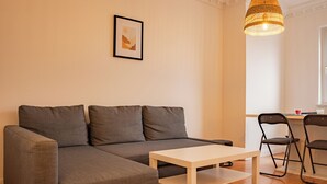 Ein modernes Wohnzimmer mit einem grauen Ecksofa, einem weißen Couchtisch und zwei schwarzen Sesseln. An der Wand hängt ein gerahmtes Bild und über dem Sofa eine Pendelleuchte.