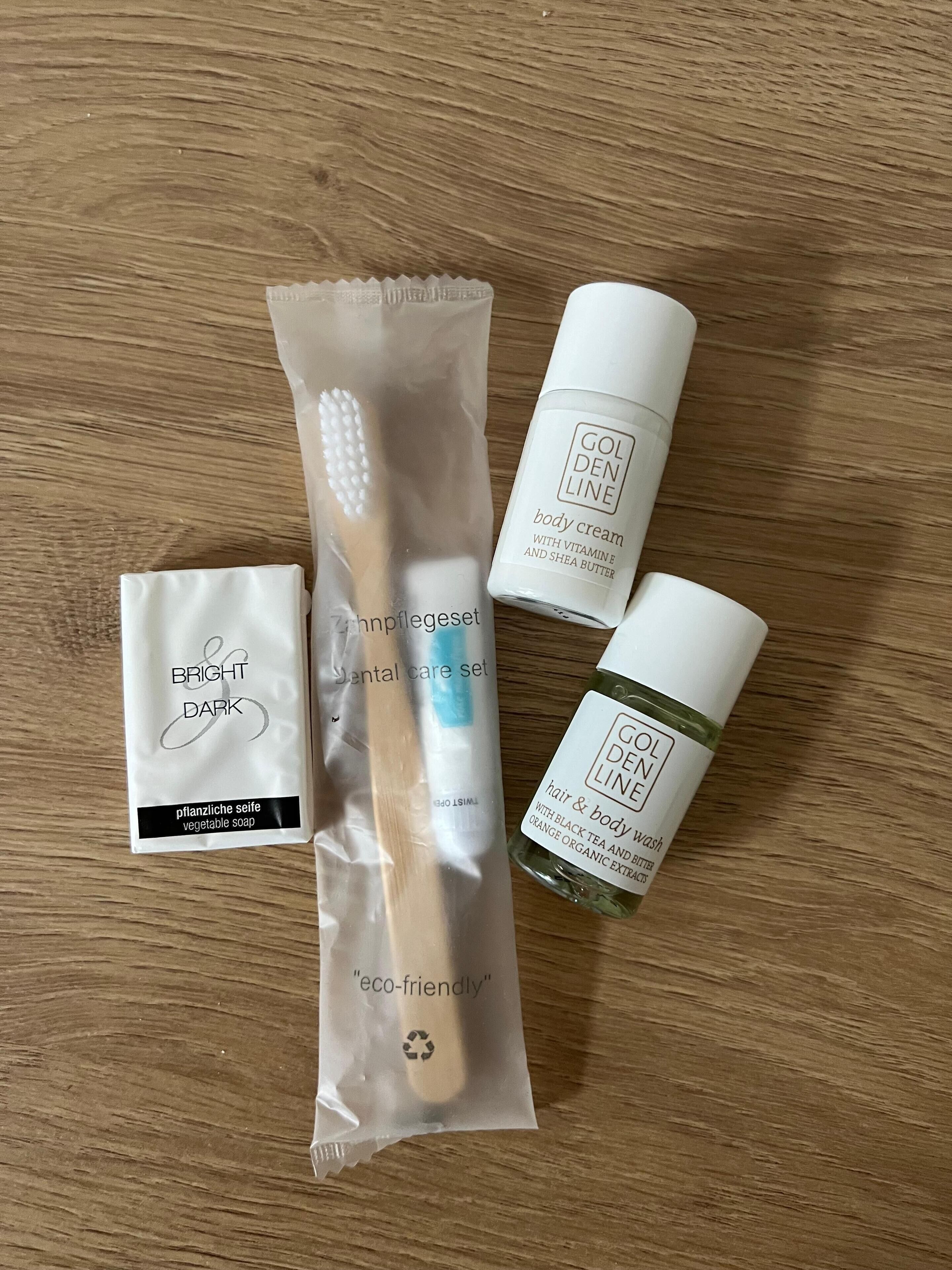 Une surface en bois sur laquelle se trouvent quatre articles : une brosse à dents, un flacon de crème pour le corps, un ensemble de produits d’hygiène bucco-dentaire et un flacon de gel douche pour les cheveux et le corps.