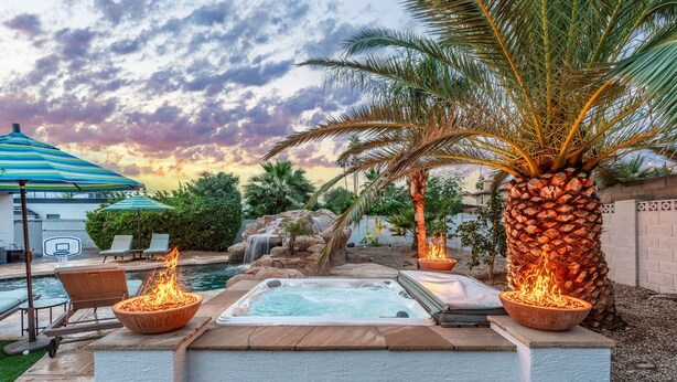 Een achtertuin met een jacuzzi, ligbedden, een palmboom en een waterval.