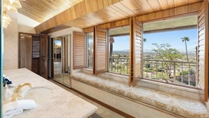 A bathroom with a large window, wooden ceiling, and a view of a cityscape.