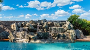 A pool with a rock waterfall, clear blue water, and a stone wall in the background.