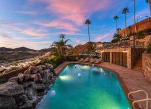 A pool with a waterfall feature, lounge chairs, and a view of a mountainous landscape.