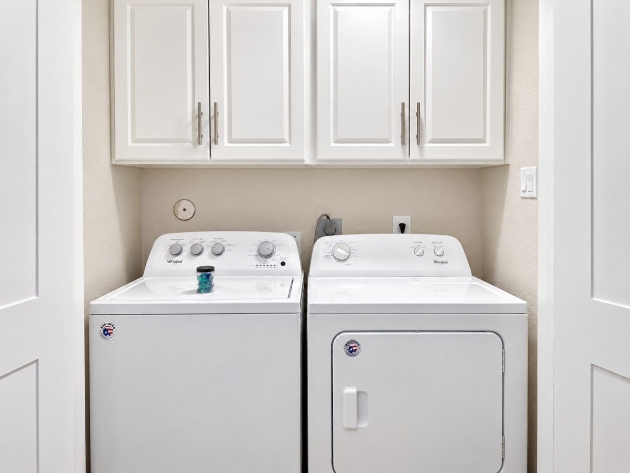 Een wasserette met twee witte Whirlpool wasmachines en drogers, een klok en een stopcontact.