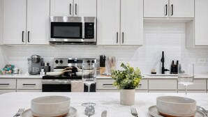 Una cocina moderna con armarios blancos, un microondas de acero inoxidable y una isla central con dos tazones y una planta en maceta.