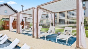 Un espace aménagé au bord de la piscine, avec des chaises longues, une petite piscine et un coin salon couvert offrant une vue sur un immeuble d’habitation.