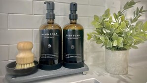 Two bottles of hand and dish soap on a shelf, a wooden brush, and a potted plant. - WorkerFriendly,Wash/Dry,WiFi, Pool,A+Location,Gym (Sherman)