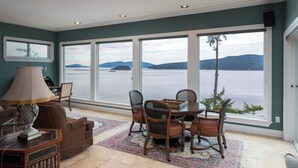 A dining area with a table and chairs, large windows with a view of a lake and mountains, and a patterned rug.