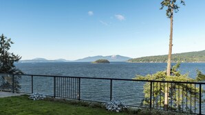 A lakeside view with a grassy area, a metal railing, and a tree.