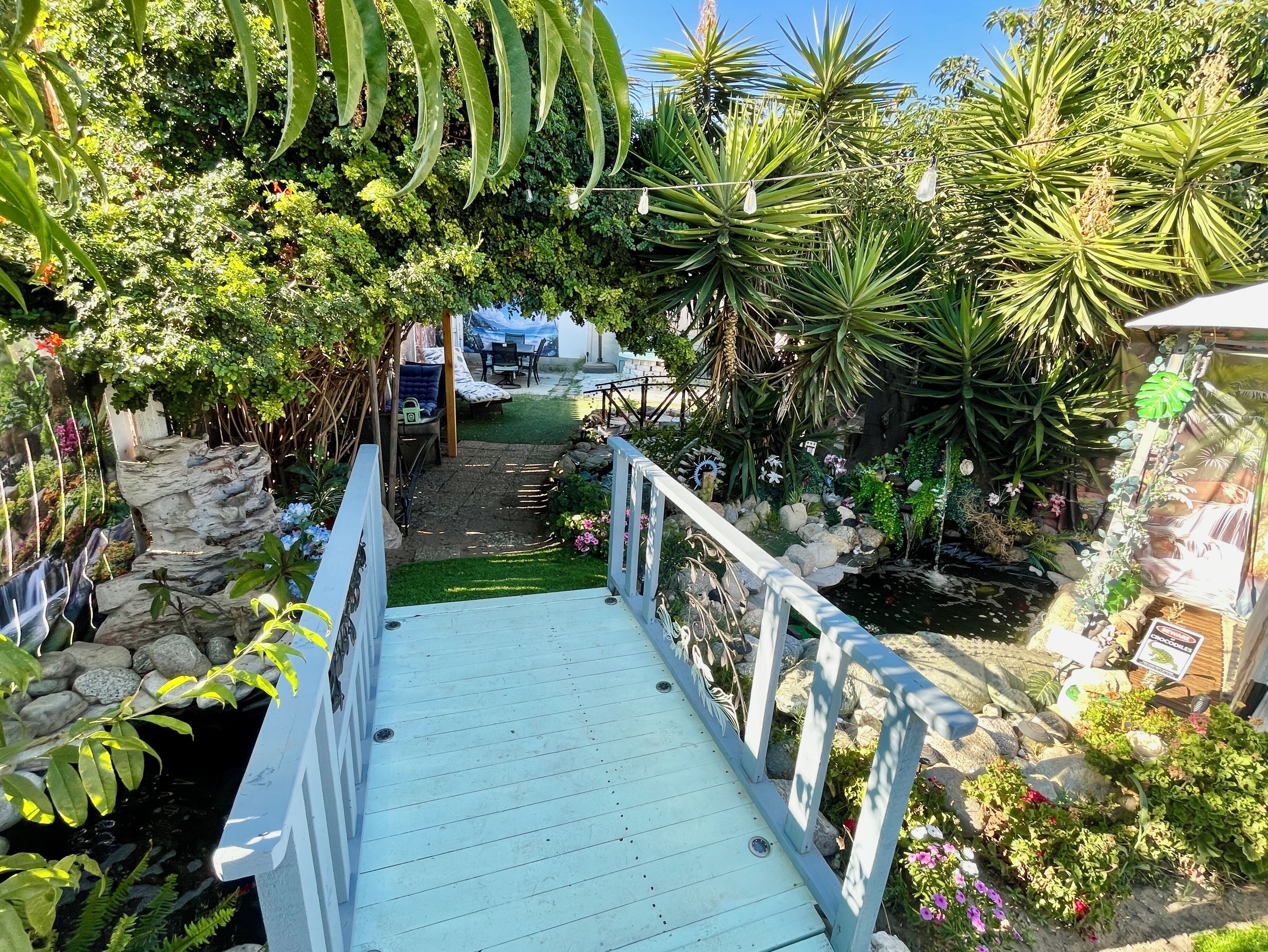 A garden pathway with a wooden deck, surrounded by various plants and a small pond.