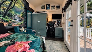 Un dormitorio con cama, escritorio, silla y vista a un jardín por la ventana.