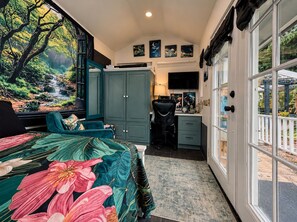 Un dormitorio con cama, escritorio, silla y vista a un jardín por la ventana.