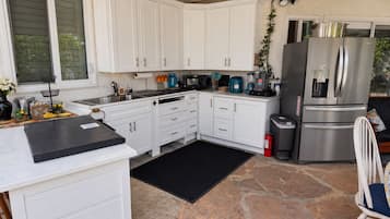 A kitchen with white cabinets, a black countertop, a stone floor, a stainless steel refrigerator, and a coffee maker.
