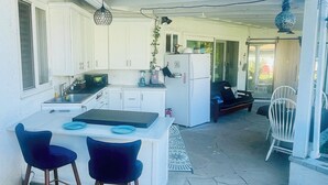 A compact kitchen with white cabinets, a refrigerator, and a dining area with two blue chairs. - KOI PONDS RETREAT 3K SqFt VILLA Outdoor Kitchen~Living 2B1Ba MASTER SUITE+CASITA (Fullerton)
