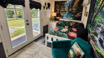 Quarto com cama, mesa de cabeceira, luminária, janela com cortinas e um quadro de uma cascata.