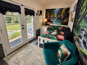 Un dormitorio con una cama, una mesita de noche, una lámpara, un ventanal con cortinas y un cuadro de una cascada.