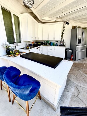 Una cocina con armarios blancos, un refrigerador de acero inoxidable, una encimera negra y taburetes de bar azules.